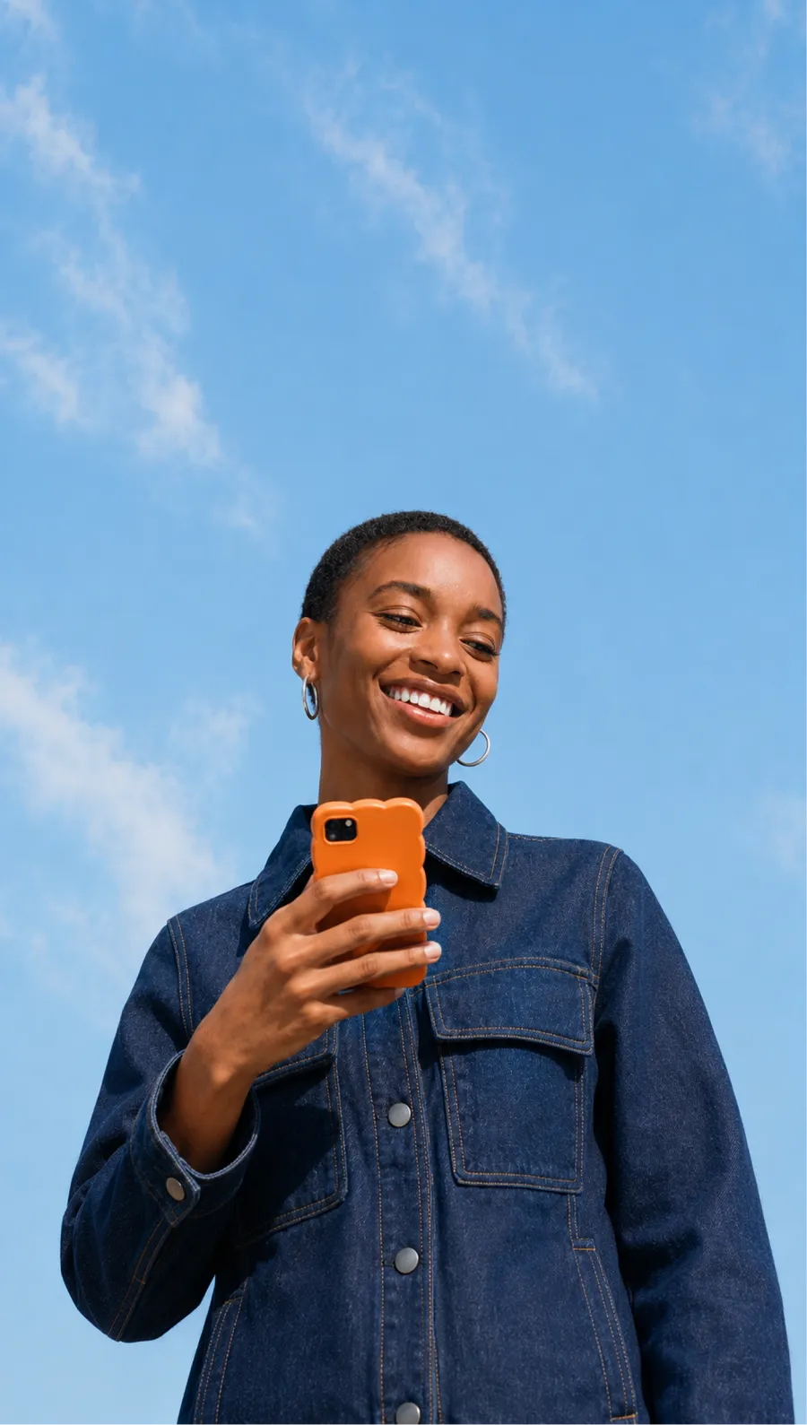 A person checking their phone outdoors under a blue sky