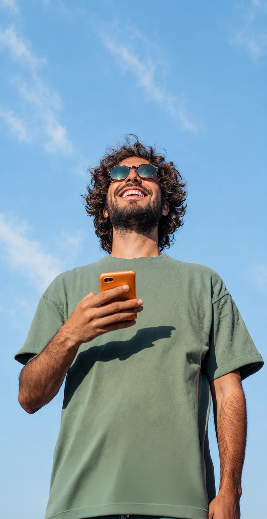 A person smiling at their phone against a clear sky